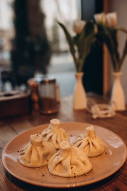 Kafede tabakta 4 Khinkali. Bulanık beyaz laleler. Masanın üzerinde bir demet çiçekli hafif vintage vazo var. .