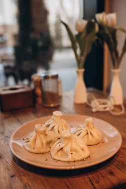 Kafede tabakta 4 Khinkali. Bulanık beyaz laleler. Masanın üzerinde bir demet çiçekli hafif vintage vazo var. .