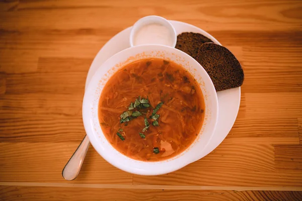 Geleneksel Ukrayna çorbası. Beyaz kase kırmızı pancar kökü çorbası ve yeşillik. Patates, et, havuç, lahana ve sarımsaklı lezzetli çorba. Geleneksel Ukrayna mutfağı kahverengi ekmek, ekşi krema