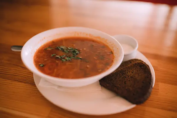 Stock image Traditional Ukrainian borsch. White Bowl of red beet root soup and greens. Sour delicious soup with potato, meat, carrot, cabbage, garlic. Traditional Ukraine food cuisine with brown bread, sour cream