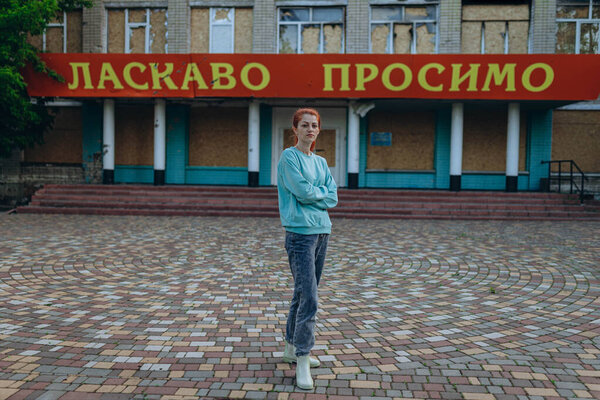 Lady stands in front of damaged and destroyed school in village after the bomb explosion. the words "Welcome" at the entrance. The war against Ukraine. Russian bomb hit the school. Terror attack. Evil