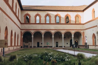 Milan, Italy- 13 Mayıs 2023: İç avlu manzarası, Castello Sforzesco antik anıtı, avlunun yeşil çimenliği, mavi gökyüzü beyaz bulutları,