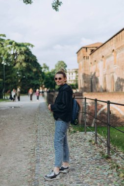 Turist kadın antik duvarların, köşe kulesinin, Castello Sforzesco antik anıtının, avlunun yeşil çimlerinin, mavi gökyüzü beyaz bulutlarının arkasında duruyor.,