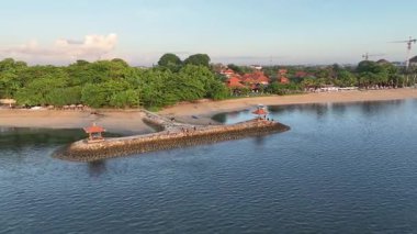 Sakin bir tropikal plajın insansız hava aracı görüntüsü. Taş iskelesi, geleneksel çardağı, tekneleri ve yemyeşil ağaçları var. Seyahat, tatil ve ada yaşam tarzı temaları için mükemmel.