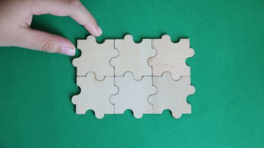 Yeşil arka planda yapboz parçasıyla oynayan bir kadın eli