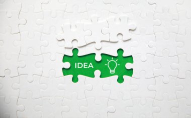 Açılmış elementlerle birleştirilmiş durumda beyaz yapboz. Fikir ve ampul simgesi ile yeşil bir alan oluşturuyor. 