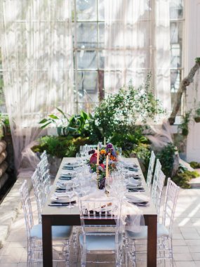 Serada düğün ziyafeti veriyorum. Masanın ortasında çiçek buketleri, altın şamdanlar ve tabaklar var. Şeffaf sandalyeler. Panoramik pencereler, yeşil bitkiler.