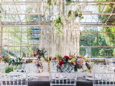 Serada ziyafet masası servis ettim. Çiçekli buketler, bir bardak şarap, tabaklar masanın üstünde. Arka planda bir panorama penceresi ve park manzarası var..