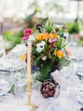 Tropikal bir düğün sofrası dekorasyonu ve servisi. Renkli bir buket enginar, beyaz ve pembe şakayık, lale, süsen çiçeği. Şarap bardakları, mumlar, çanak çömlek takımı, çatal bıçak takımı..