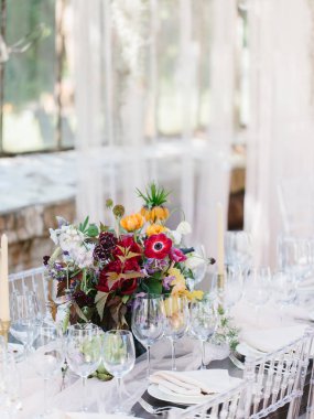 Tropikal bir düğün sofrası dekorasyonu ve servisi. Renkli bir buket enginar, beyaz ve pembe şakayık, lale, süsen çiçeği. Şarap bardakları, mumlar, çanak çömlek takımı, çatal bıçak takımı..