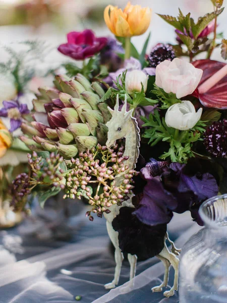 A colorful bouquet of artichoke, white and pink peonies, tulips, iris. Wedding banquet table decor, giraffe figurine.
