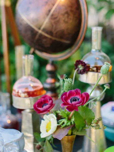 Outdoor party decor. In the foreground is a bouquet of pink and white poppies. Decor from flasks with cocktails, vintage globe.