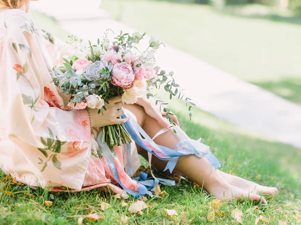 Panna Młoda Różowym Szlafroku Kwiatami Siedzi Trawniku Posiada Bukiet Ślubny — Zdjęcie stockowe