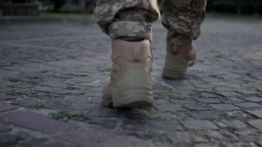 Legs of young man in military uniform walking slowly down the street on a sunny day. Human legs in military boots. Back view legs of Ukrainian female soldier in camouflage uniform. 