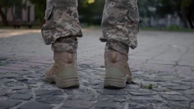 Legs of young man in military uniform walking slowly down the street on a sunny day. Human legs in military boots. Back view legs of Ukrainian female soldier in camouflage uniform. 