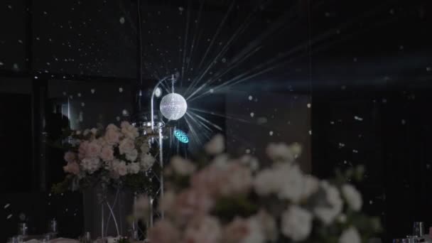 結婚式のフラワーアレンジメントの背景にディスコ層 回転層は光線をミラーします 宴会場 フラワーアレンジメント付きテーブル — ストック動画