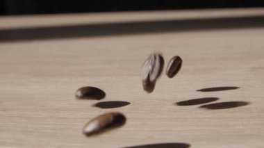 Kahve çekirdekleri düz ahşap zemine düşüyor. Ahşap masa yüzeyine düşen kavrulmuş kahve çekirdekleri. Kahve çekirdekleri zıplıyor. - Yakın çekim. Yavaş çekim.