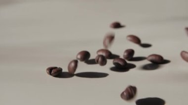 Kahve çekirdekleri hafif bir yüzeye düşüyor. Kavrulmuş kahve çekirdekleri ışık yüzeyine düşüyor. Kahve çekirdekleri zıplıyor. - Yakın çekim. Yavaş çekim.