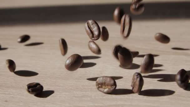 平らな木製の表面に落ちるコーヒー豆 木製のテーブルの表面に落ちるローストコーヒー豆 木製の板の表面に振りかける茶色のローストコーヒー豆 閉鎖だ スローモーション — ストック動画
