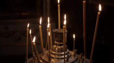 Ortodoks kilisesinde mumlar yanar. Mumlar karanlıkta karanlıkta, arka plandaki karanlık kamera hareketlerine karşı yanar. Kilise mumları kilisedeki büyük altın bir şamdanda yanar. Yavaş çekim.
