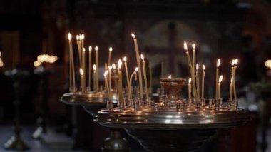 Ortodoks kilisesinde mumlar yanar. Mumlar karanlıkta karanlıkta, arka plandaki karanlık kamera hareketlerine karşı yanar. Kilise mumları kilisedeki büyük altın bir şamdanda yanar. Yavaş çekim.