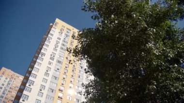 Mavi gökyüzü arka planındaki çok katlı bir binanın alçak açılı görüntüsü. İnşa edilmiş evler. Çok katlı binalar. Çok katlı binanın dış cephesi. Bir sürü yeşil alan var..