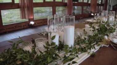 Düğün masasında çiçek aranjmanı. Düğün masasının açık renkli, yeşillikli ve mumlu süslemeleri. Bir ziyafet masası için çiçek düzenlemeleri.