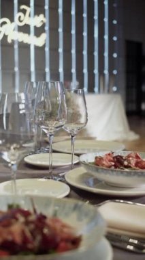 Garson elinde salata olan bir tabak servis ediyor. Arka planda da da şenlikli bir düğün masası var. Garsonun elleri masaya bir tabak salata koydu. Dikey video.