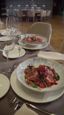 Garson elinde salata olan bir tabak servis ediyor. Arka planda da da şenlikli bir düğün masası var. Garsonun elleri masaya bir tabak salata koydu. Dikey video.