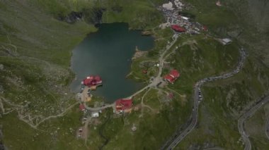Romanya 'nın Transfagarasan yolundaki Balea Gölü' nün insansız hava aracı görüntüleri. Video gölün yukarısından çekilmiş. Kamera gölün, kulübelerin ve kavisli yolun üst görüntüsü için eğilmiş..