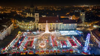 Sibiu şehir merkezinin Noel Fuarı 'yla çekilmiş peyzaj fotoğrafçılığı. Gün batımında şehir yıldırımı açıkken bir drondan çekilmiş. Romanya 'nın Sibiu kentinin manzarasına kuşların bakışı.