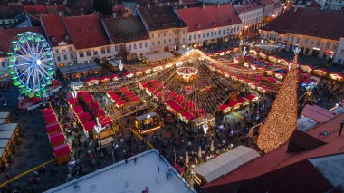 Sibiu şehir merkezinin Noel Fuarı 'yla çekilmiş peyzaj fotoğrafçılığı. Gün batımında şehir yıldırımı açıkken bir drondan çekilmiş. Romanya 'nın Sibiu kentinin manzarasına kuşların bakışı.