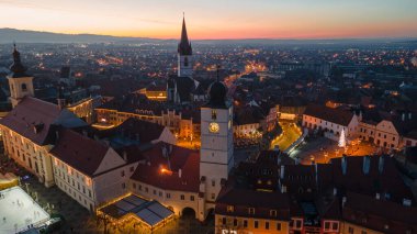 Sibiu şehir merkezinin Noel Fuarı 'yla çekilmiş peyzaj fotoğrafçılığı. Gün batımında şehir yıldırımı açıkken bir drondan çekilmiş. Romanya 'nın Sibiu kentinin manzarasına kuşların bakışı.