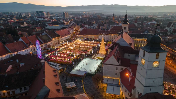 Sibiu şehir merkezinin Noel Fuarı 'yla çekilmiş peyzaj fotoğrafçılığı. Gün batımında şehir yıldırımı açıkken bir drondan çekilmiş. Romanya 'nın Sibiu kentinin manzarasına kuşların bakışı.