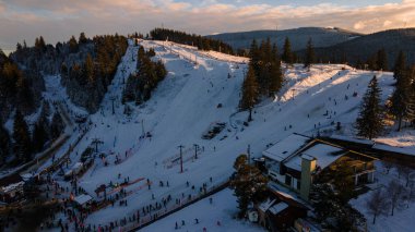 Aerial view of a skying slope on top of the mountain in winter season at sunset. Photography was shot from a drone at a higher altitude. Aerial view of a resort with skying slope in winter at sunset