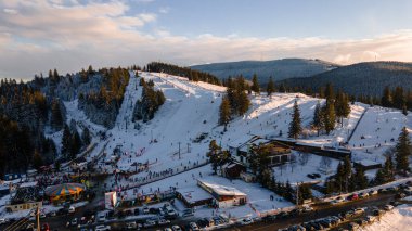 Aerial view of a skying slope on top of the mountain in winter season at sunset. Photography was shot from a drone at a higher altitude. Aerial view of a resort with skying slope in winter at sunset