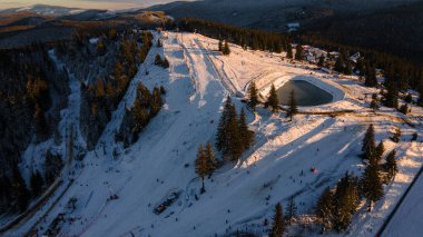 Aerial view of a skying slope on top of the mountain in winter season at sunset. Photography was shot from a drone at a higher altitude. Aerial view of a resort with skying slope in winter at sunset