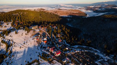 Aerial view of a small resort on top of the mountain in winter season at sunset. Photography was shot from a drone at a higher altitude. Aerial view of a resort in winter at sunset