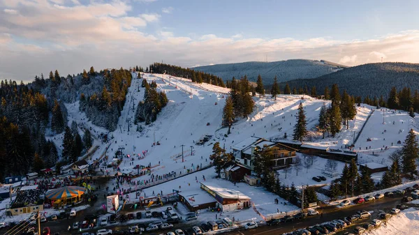 Aerial view of a skying slope on top of the mountain in winter season at sunset. Photography was shot from a drone at a higher altitude. Aerial view of a resort with skying slope in winter at sunset