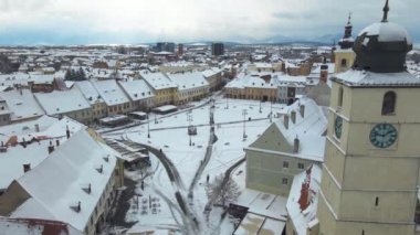 Aerial view of the medieval city center of Sibiu, Romania in winter at sunset. The footage was made from a drone at a lower altitude while banking right with the Town Hall tower in the view. 