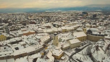 Aerial view of the medieval city center of Sibiu, Romania in winter at sunset. The footage was made from a drone while lowering altitude and flying forward towards the town hall tower.