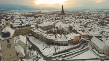 Aerial view of the medieval city center of Sibiu, Romania in winter at sunset. The footage was made from a drone while flying backwards with the Evangelic Cathedral and the Hall tower  in view.