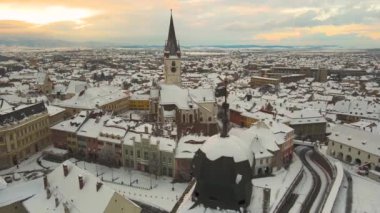 Romanya 'nın Sibiu kentinin ortaçağ şehir merkezine kışın günbatımında hava manzarası. Görüntüler, eski kasaba binalarının üzerinde dairesel bir yörüngede uçarken düşük irtifadaki bir drondan çekilmiş..