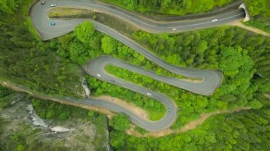 Dağlardaki dolambaçlı bir yolun havadan görüntüsü, yüksek irtifadaki bir drondan çekilen görüntü ve yüksek bir görüntü için alçak kamera açısı. Romanya 'nın Bicaz bölgesindeki dağlarda bir yılan yolunun videosu.