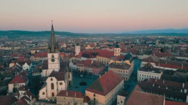 Günbatımında Romanya 'nın Sibiu kentindeki ortaçağ şehir merkezinin insansız hava aracı görüntüleri. Video, güneş batarken bir İHA 'dan, panoramik görüntü için kamera seviyesiyle Katedral' e doğru uçarken çekilmiş..
