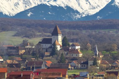 Romanya 'nın Sibiu kentindeki Hosman kentindeki güçlendirilmiş kilisenin fotoğrafları, arka planda Fagaras dağları ile birlikte gün ortasında çekildi..