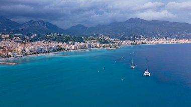 Menton, Fransa 'daki Fransız Rivierası' nın hava görüntüsü. Fotoğraf, daha yüksek bir irtifada, körfezin yukarısından, arka planda fırtınalı bir havada şehir ve dağlarla çekilmiş..