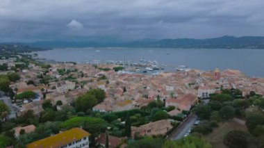 Saint-Tropez ve marinanın havadan görüntüsü. Görüntüler, bulutlu bir günde arka planda körfez olan yüksek irtifadaki bir drondan çekildi. Video tatil köyünün yukarısındaki bir İHA 'dan çekilmiş..