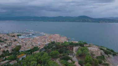 Saint-Tropez 'in havadan görünüşü marina ve kale. Görüntüler, bulutlu bir günde, arka planda körfez ile geriye doğru uçarken, daha yüksek bir irtifadaki bir drondan çekildi.. 