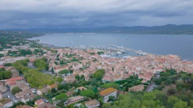 Saint-Tropez ve marinanın havadan görüntüsü. Görüntüler, bulutlu bir günde arka planda körfez olan yüksek irtifadaki bir drondan çekildi. Video tatil köyünün yukarısındaki bir İHA 'dan çekilmiş..